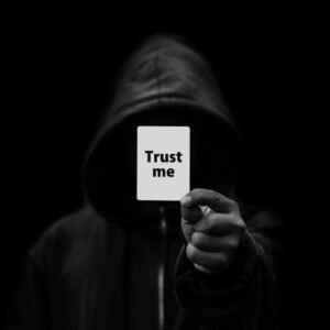Silhouette dans le noir encapuchonnée tient un papier 'aies confiance', la double face des manipulateurs obscurs et souriants
