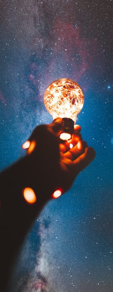Une main tendue vers le ciel entourée d'une guirlande lumineuse & au bout une ampoule allumée illustrant la pleine conscience