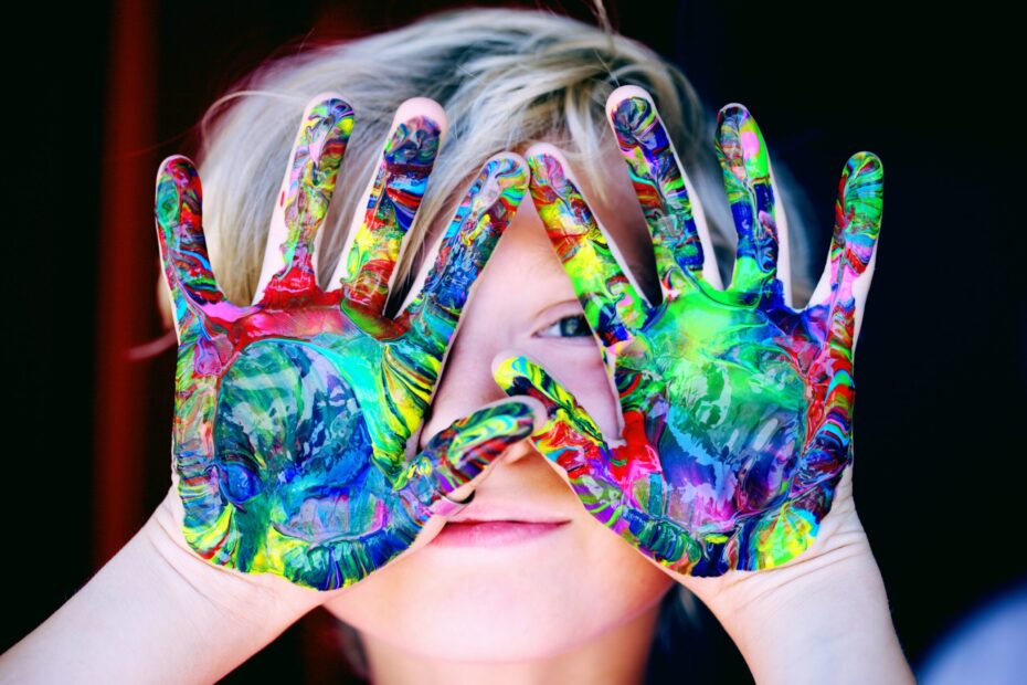 Un enfant se cache le visage avec les mains pleine de peinture multicolore, l'éveil passe par la motricité et l'apprentissage